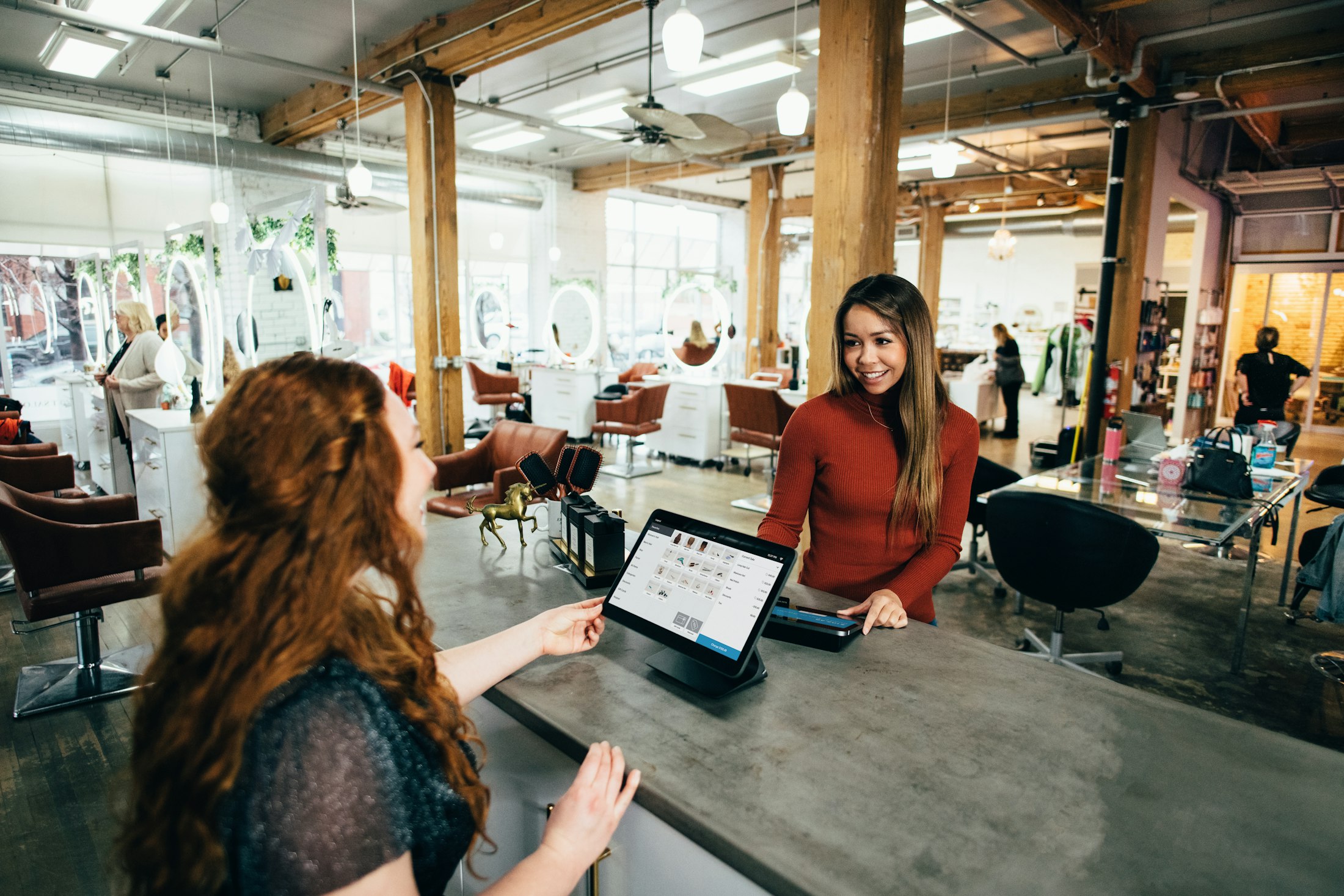 An independent salon at the counter — a customer paying while the owner rings the sale through on a tablet